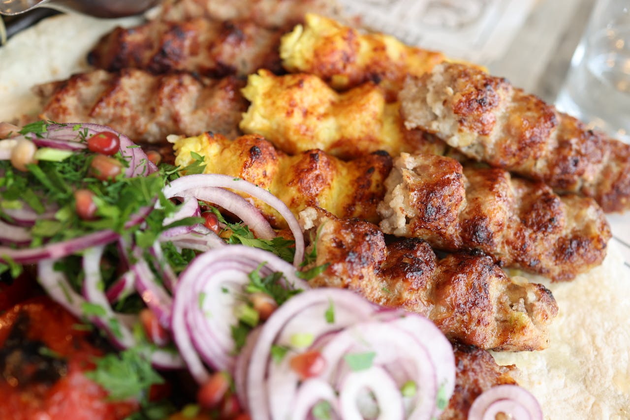 Close-up of assorted grilled meat kebabs with fresh herbs and red onion slices, ready to serve.