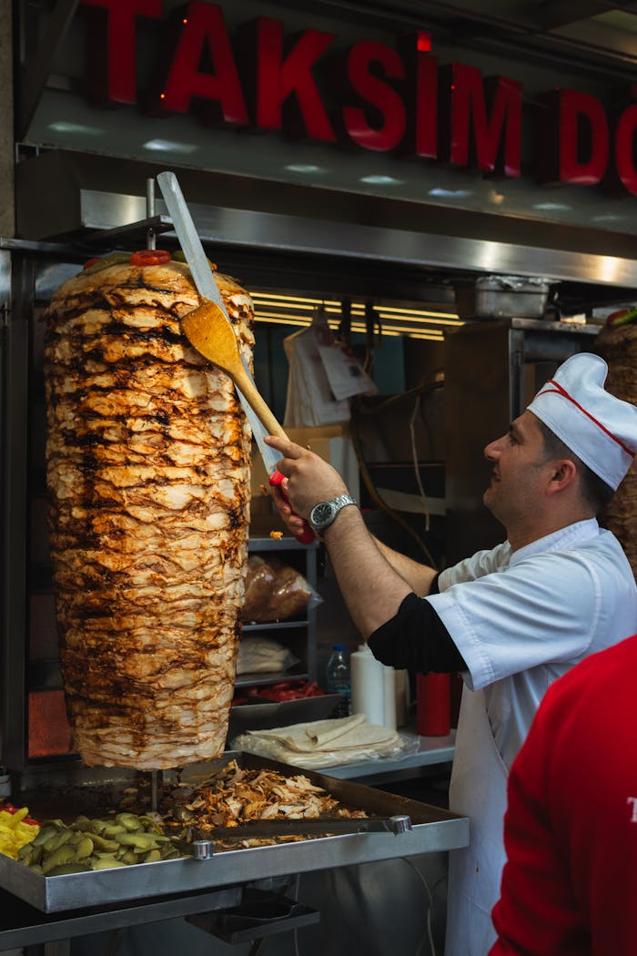 A chef preparing a traditional döner kebab in a busy Turkish restaurant, slicing the meat vertically.