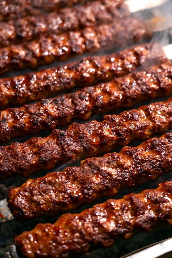 Close-up of sizzling meat kebabs on a grill with smoke rising, perfect for barbecue enthusiasts.