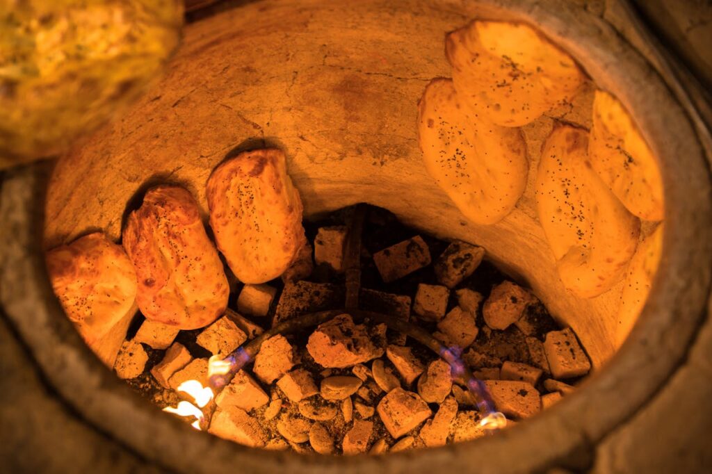 Close-up of naan bread baking in a tandoor oven with visible flames and coals.